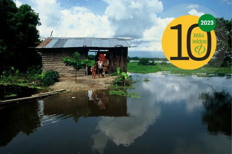 Mujer y niños frente a una casa precaria en tierra inundada en Colombia.