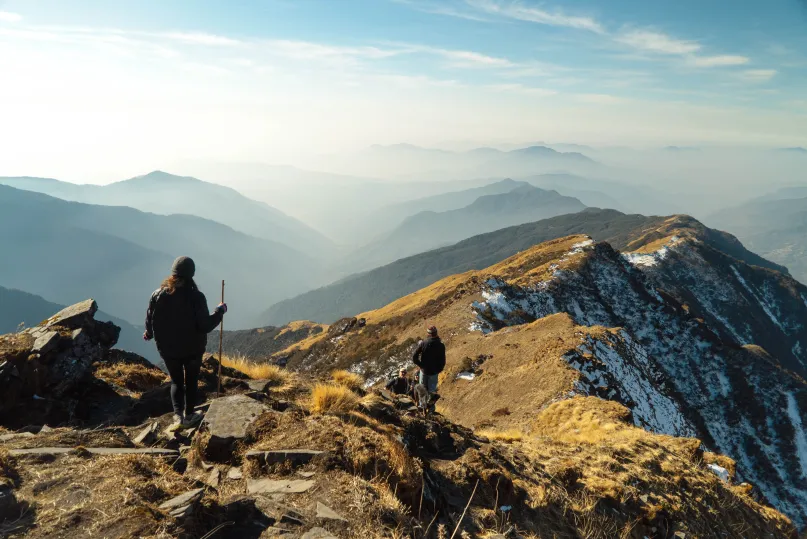 Hikers traversing a mountain ridge with several peaks in the background.