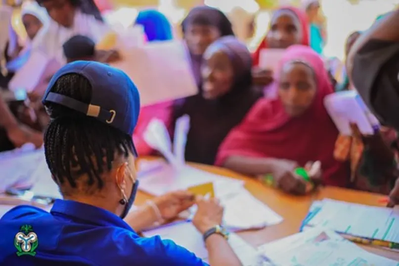 Many women sitting at a desk with bank official.