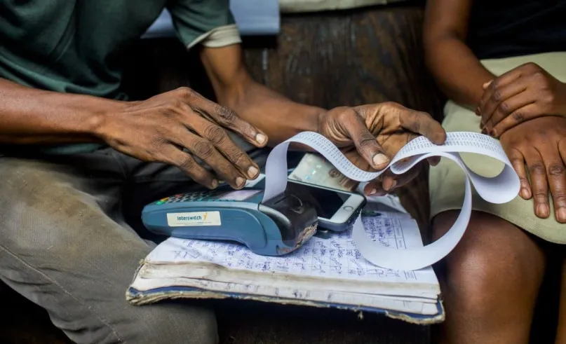 Hands working on a calculator with a mobile phone next to it on top of a notebook.