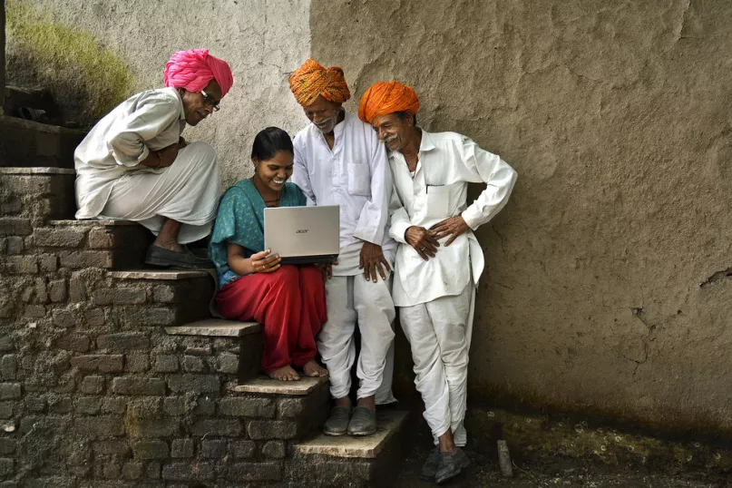 Woman with laptop showing farmers market prices, India. 