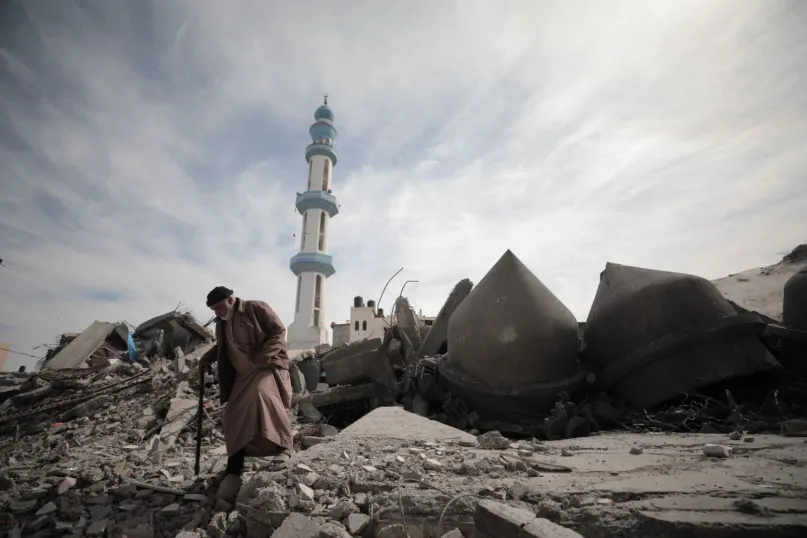 Older man wearing robe walking through destruction in Gaza.