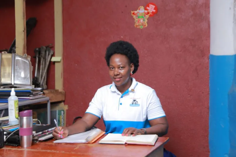 African woman sitting at desk, holding pen with notebook open.