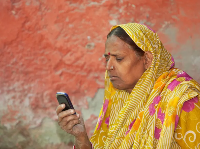 Indian woman in yellow sari looking at a feature phone.