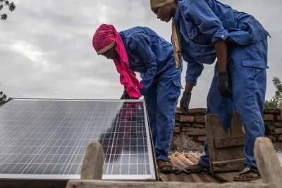 Two workers in blue uniforms installing a solar panel