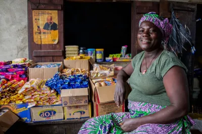 Woman seated in front of her shop with goods displayed in cardboard boxes.