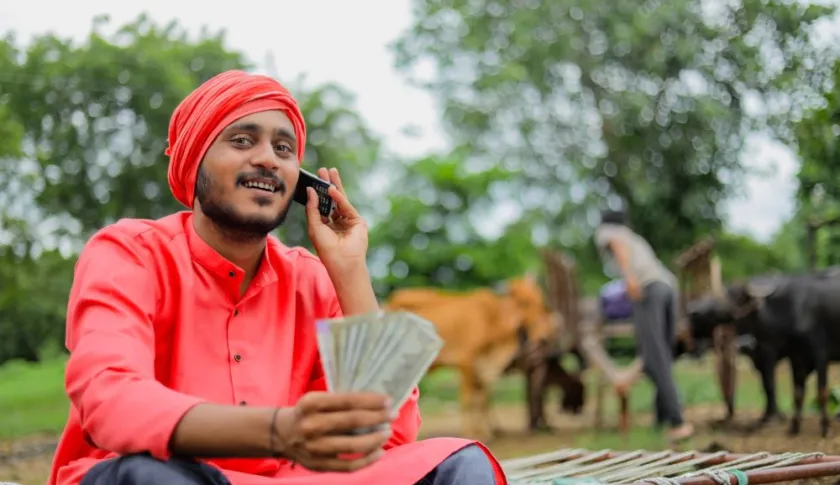 Man with red turban holding phone to ear and holding currency.