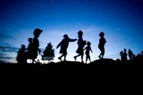 Siluetas de personas acarreando bultos con el cielo del atardecer de fondo en Haití.